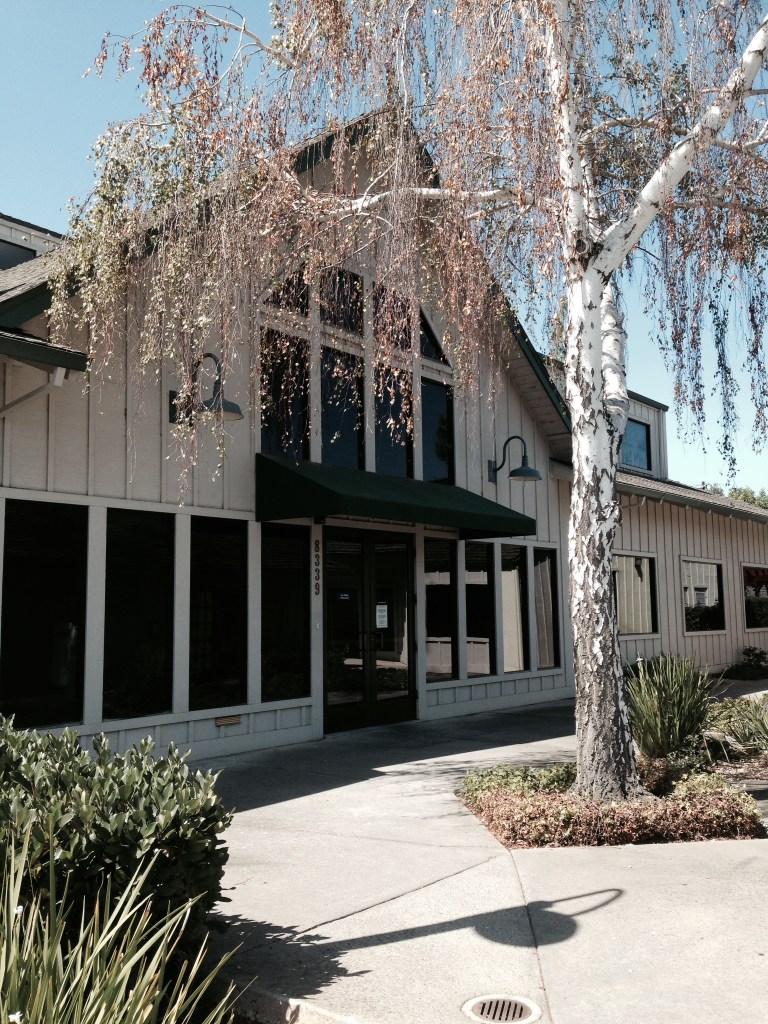 Photo of the front of the new Lincoln office. It's a white building with a black umbrella awning over a double front door.